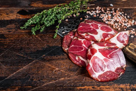 Coppa, Capocollo, Capicollo Cured ham on meat cleaver. Dark wooden background. Top view. Copy space.
