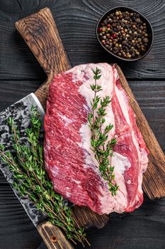 Fresh Raw Round roast beef meat cut on a butcher cutting board with cleaver. Black wooden background. Top view.