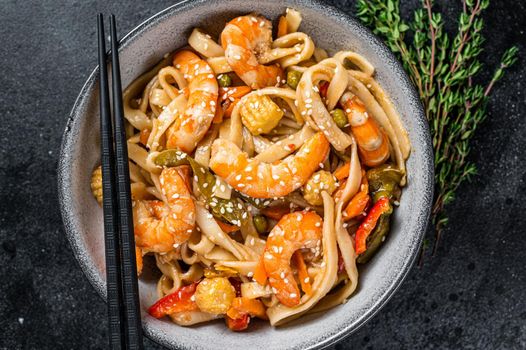 Stir-fry udon seafood noodles with shrimp prawns in a bowl. Black background. Top view.