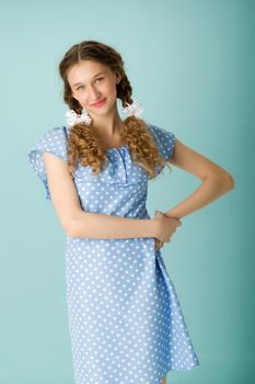 Portrait of a cheerful teenage girl in a blue dress. Happy girl in polka dot dress looking up with positive facial expression over isolated blue background.close-up