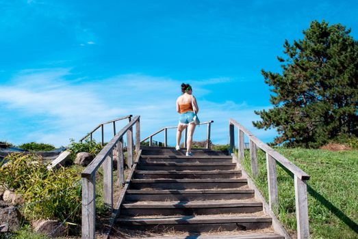 Rear view of a young woman in short shorts climbing stairs in a summer park on a sunny day.