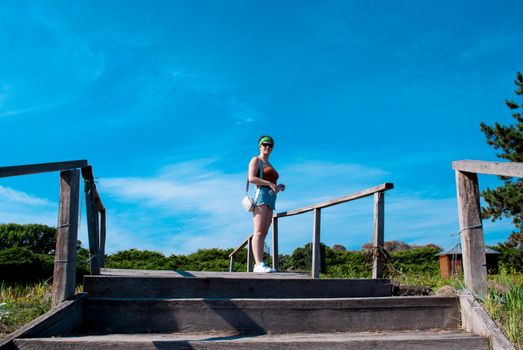 Rear view of a young woman in short shorts climbing stairs in a summer park on a sunny day.