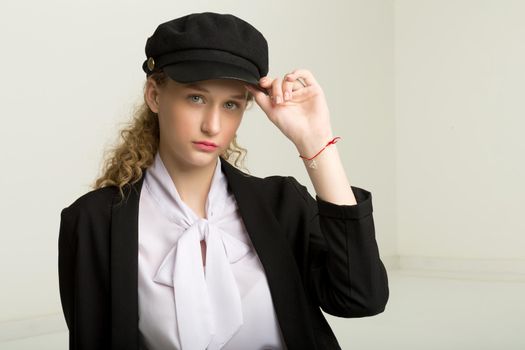 Portrait of pretty girl in black suit and cap. Beautiful stylish young woman in fashionable black blazer, white blouse and cap looking seriously at camera posing against gray background in studio