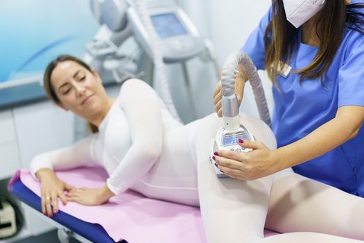 Middle-aged woman in special white suit having a anti cellulite massage with spa apparatus