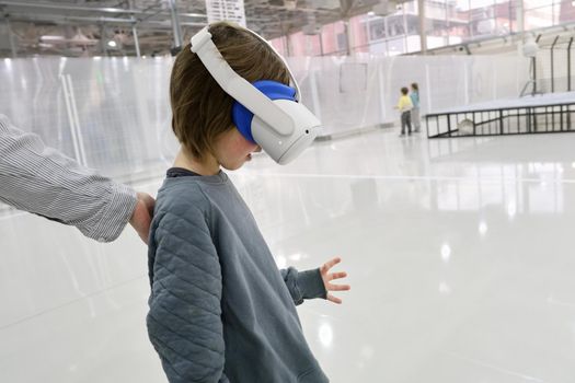 Side view of boy wearing modern VR goggles immersing in cyberspace in spacious showroom