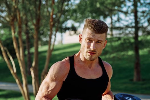 athletic man in black t-shirt with dumbbells in the park training. High quality photo