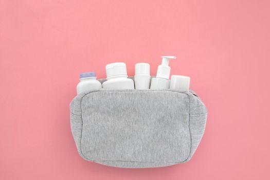 White bottles of cleansing cosmetics in cosmetic bag. Beautiful cosmetic and creams set from cosmetic bag on pink background copyspace. Minimalism cosmetics style top view, flat lay