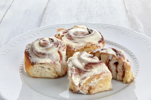 High angle of bunch of fresh cinnamon rolls with sweet icing placed on elegant ceramic plate