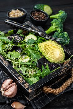 Vegetarian green salad with salad leaves mix, avocado and vegetables. Black Wooden background. Top view.
