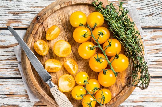 Sliced yellow cherry tomato on a wooden tray with herbs. White wooden background. Top view.