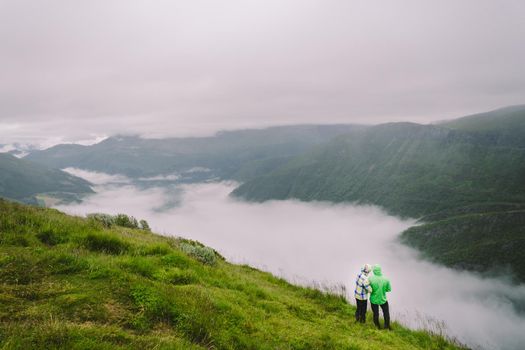 Hiking in Norway. Romantic couple of tourists on the edge of cliff looking on beautiful scenery. Back view of couple hugging at observation deck with panoramic view. Traveling together, adventure.