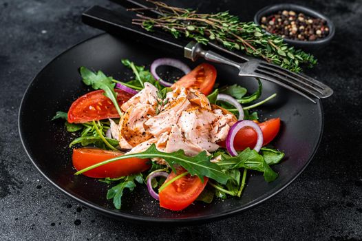 Salad with roasted salmon fillet steak, fresh salad arugula and tomato in a plate. Black background. Top view.