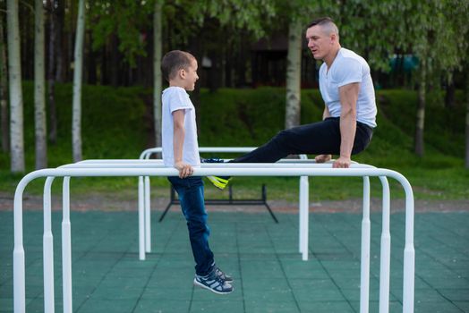 Caucasian man trains a boy on the uneven bars on the playground. Dad and son go in for outdoor sports