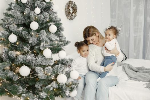 People reparing for Christmas. Mother playing with her daughters. Family is resting in a festive room. Child in a sweater sweater.