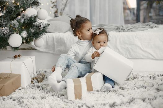 Child in a white sweater. Daughters stitting near Christmas tree.Two sisters at home.