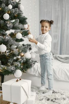 Child in a white sweater. Daughter standing near Christmas tree.