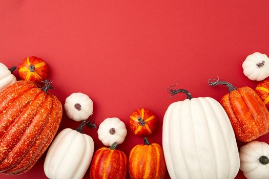 Different size white and orange pumpkins top view against red background copy space