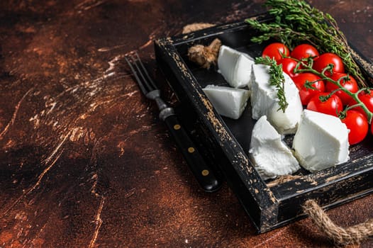 Ricotta cream Cheese in a wooden tray with basil and tomato. Dark background. Top view. Copy space.