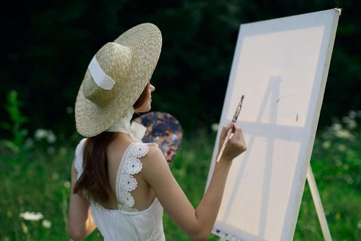 Woman in white dress paints a picture on nature easel. High quality photo