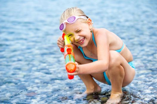 Adorable little girl is swimming in the sea and playing with a water gun. Turkey.