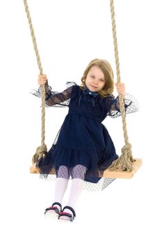Lovely blonde little girl swinging on rope swing. Sweet beautiful girl wearing nice blue dress sitting on wooden swing on isolated white background.