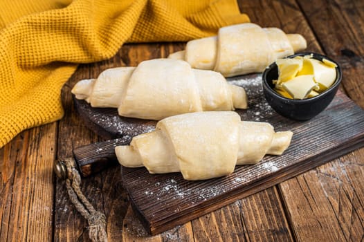 Raw uncooked french croissant on a wooden board. Wooden background. Top view.