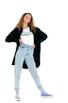 Beautiful girl in fashion outfit posing in studio. Full length shot of curly girl wearing checkered shirt, jeans and white t-shirt standing with hands on her waist on isolated white background