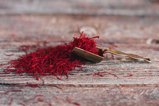 Dried saffron spice in vintage oriental metal spoon on wooden table.