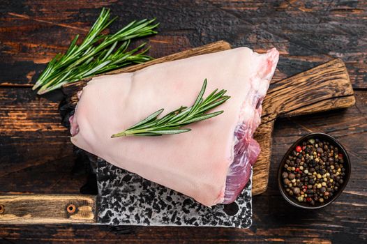 Raw pork Eisbein knuckle ham on a wooden board with meat cleaver. Dark Wooden background. Top view.