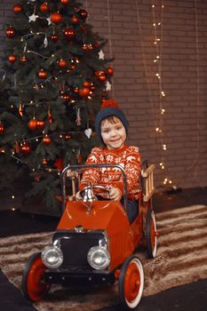 Cute little boy in a red sweater. Child by the christmas tree. Kid with toys car.