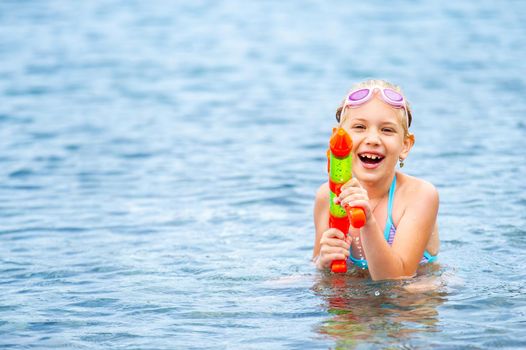 Adorable little girl is swimming in the sea and playing with a water gun. Turkey.