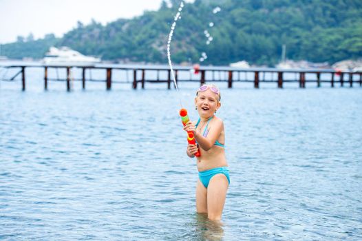 Adorable little girl is swimming in the sea and playing with a water gun. Turkey.