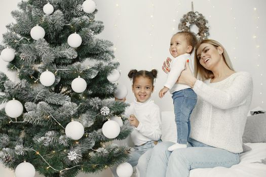 People reparing for Christmas. Mother playing with her daughters. Family is resting in a festive room. Child in a sweater sweater.