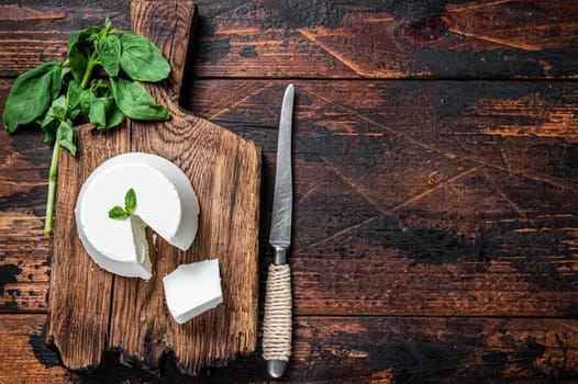 Fresh Ricotta cream Cheese on wooden board with basil. Dark wooden background. Top view. Copy space.