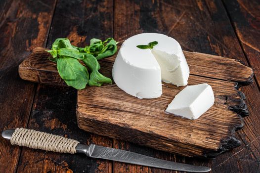 Fresh Ricotta cream Cheese on wooden board with basil. Dark wooden background. Top view.