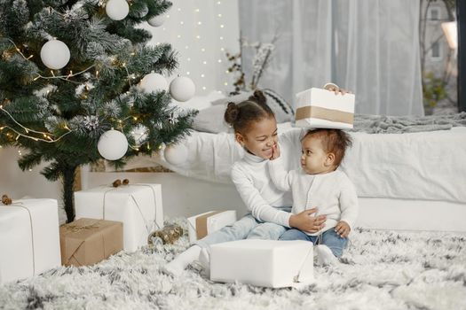 Child in a white sweater. Daughters stitting near Christmas tree.Two sisters at home.