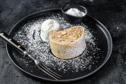 Apple strudel with cinnamon, powdered sugar and vanilla ice cream on a plate. Black background. Top view.