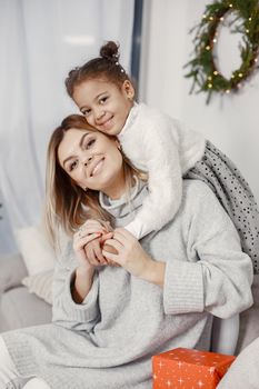 People reparing for Christmas. Mother playing with her daughter. Family is resting in a festive room. Child in a sweater sweater.