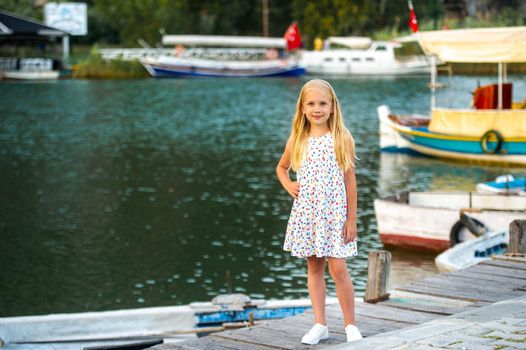 A little girl on the embankment by the river in a white sundress in the city of Dalyan. Turkey.