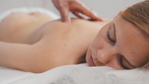 Spa. Massage for blonde woman model - man's hand on girl's back, close up view