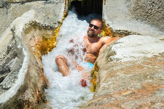 A man with glasses sits under a waterfall of healing water with thermal springs in Pamukkale.Turkey.