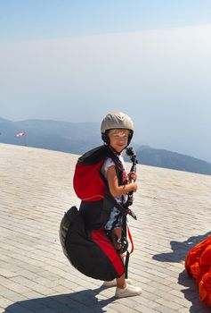 A little girl in paragliding gear and with a camera stands on the edge of Mount Babadag.Turkey.
