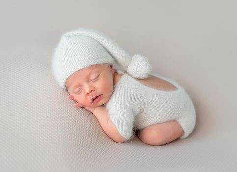 Cute little baby in white hat and knitted suit with toy sweetly sleeping