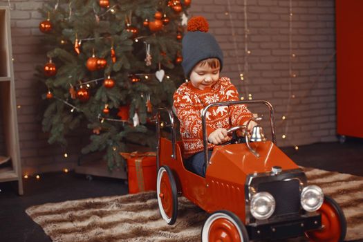 Cute little boy in a red sweater. Child by the christmas tree. Kid with toys car.