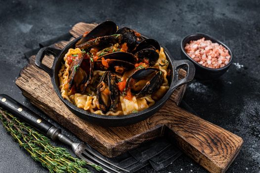 Mafaldine pasta with mussels and tomato sauce. Black background. Top view.