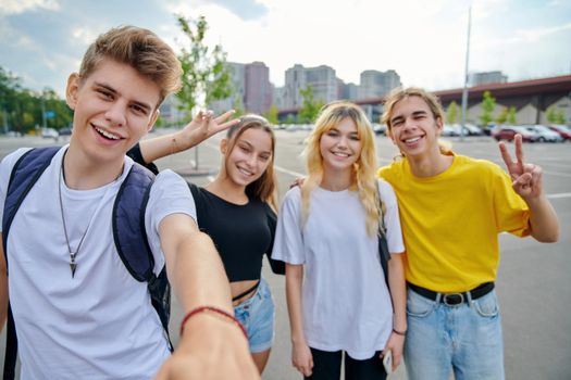 Smiling group of teenagers taking selfie, happy four teens looking at camera, city urban background. Fun, friendship, lifestyle, leisure, summer, adolescence, students concept