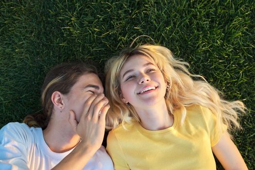 Happy couple of teenagers on green grass. Close-up of smiling faces of guy and girl 16, 17 years old, top view. Youth, adolescence, happiness, relationship, lifestyle, young people concept