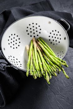 Fresh baby green asparagus in a colander. Black background. Top view.