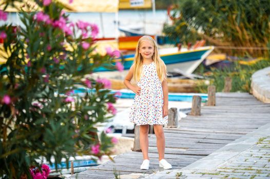 A little girl on the embankment by the river in a white sundress in the city of Dalyan. Turkey.