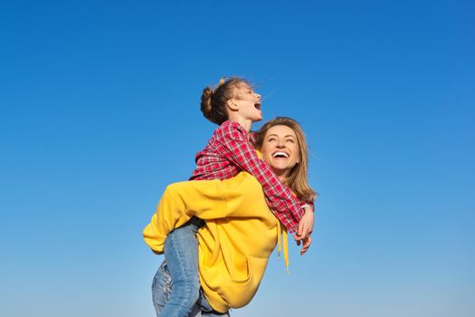 Happy mom and daughter child on seashore, relaxing on sandy beach, autumn winter spring season, copy space, blue sky background. Family vacation, travel, parent child relationship, happiness, joy